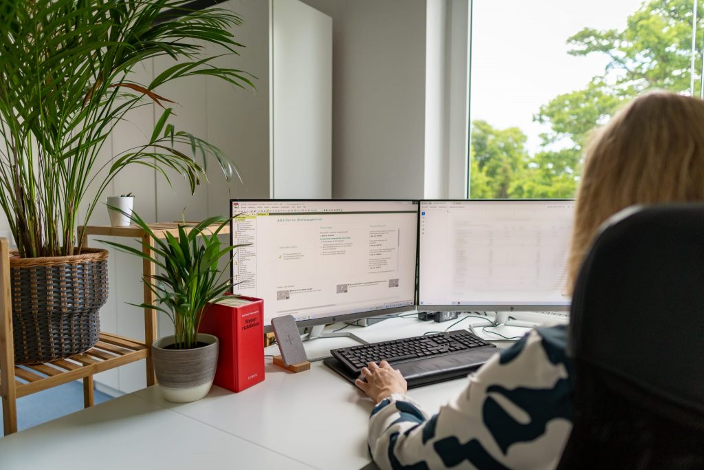 Franziska Berger am Schreibtisch mit zwei Monitoren und Pflanze – moderne Steuerkanzlei in Starnberg