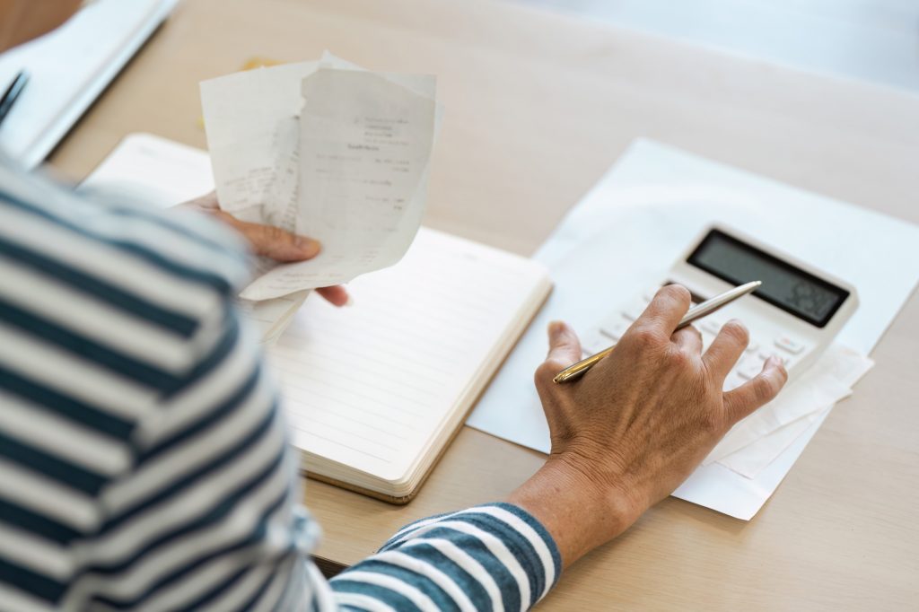 Senior Retirement Planning - Elderly Person Calculating Finances with Calculator and Receipts at
